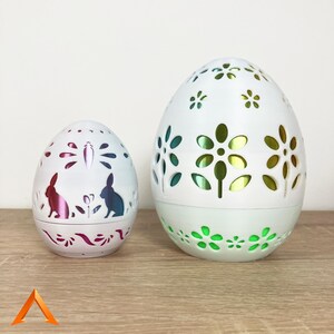 Pode incluir: Dois ovos de Páscoa de cerâmica branca com desenhos florais intrincados. O ovo maior tem um brilho verde, enquanto o ovo menor tem um brilho rosa.