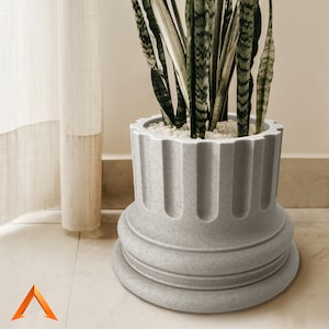 Op de afbeelding: Een grijze, gegroefde, cilindrische plantenpot met een brede basis, met daarin een groene slangplant met lange, puntige bladeren.