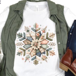 May include: White long-sleeve shirt with a colorful snowflake design. The snowflake is composed of floral and geometric patterns in shades of pink, blue, and green. The shirt is paired with a green vest, blue jeans, and brown boots.