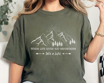 May include: A green t-shirt with a white graphic of mountains and the text "When life gives you mountains take a hike".
