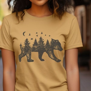 May include: A mustard yellow t-shirt with a black silhouette of a bear. The bear is made up of trees and a crescent moon. There are small birds flying above the trees.