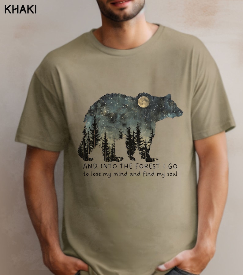 Pu&ograve; includere: T-shirt color kaki con la silhouette di un orso con una luna e stelle al suo interno. Il testo "AND INTO THE FOREST I GO to lose my mind and find my soul" &egrave; stampato sotto l'orso.