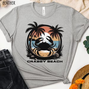 May include: A gray t-shirt with a graphic of a crab on a beach with palm trees and the text "Crabby Beach".