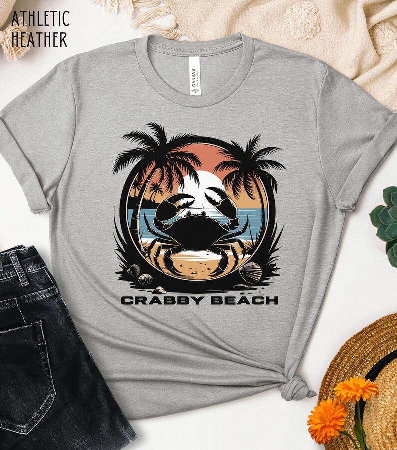 May include: A gray t-shirt with a graphic of a crab on a beach with palm trees and the text "Crabby Beach".