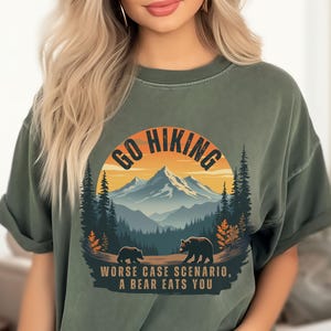 May include: Green t-shirt with a graphic of a mountain range and two bears. The graphic has the text "Go Hiking" and "Worse Case Scenario, A Bear Eats You".