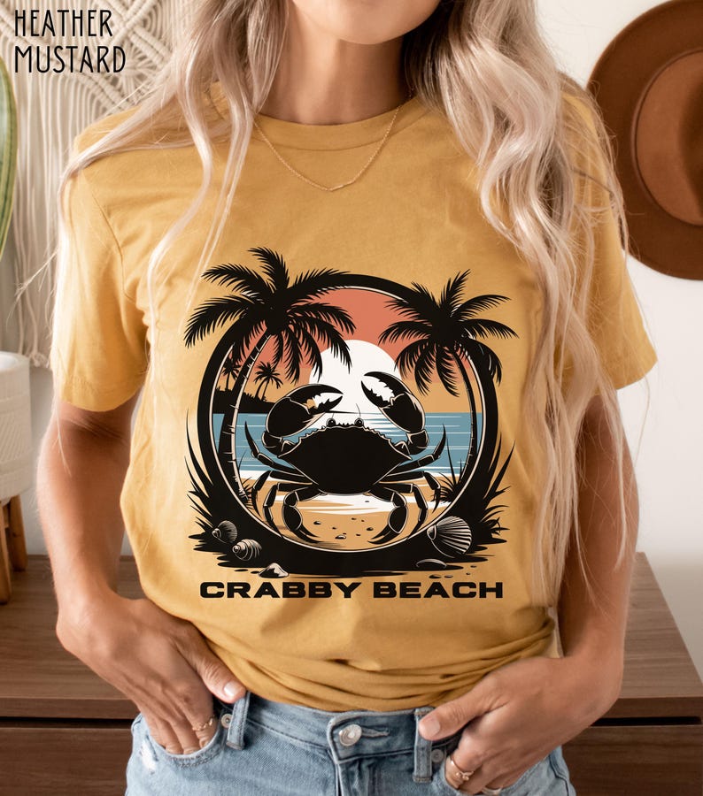 May include: A mustard yellow t-shirt with a graphic of a crab on a beach with palm trees and a sunset. The text "Crabby Beach" is printed below the graphic.