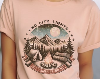 May include: Peach colored t-shirt with a vintage graphic design of a mountain scene with a campfire, tent, and the text "No City Lights, Just Campfire Nights".