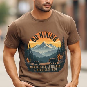 May include: A brown t-shirt with a graphic of a mountain range and the text "Go Hiking" in a circle. The graphic also includes two bears and the text "Worse case scenario, a bear eats you".
