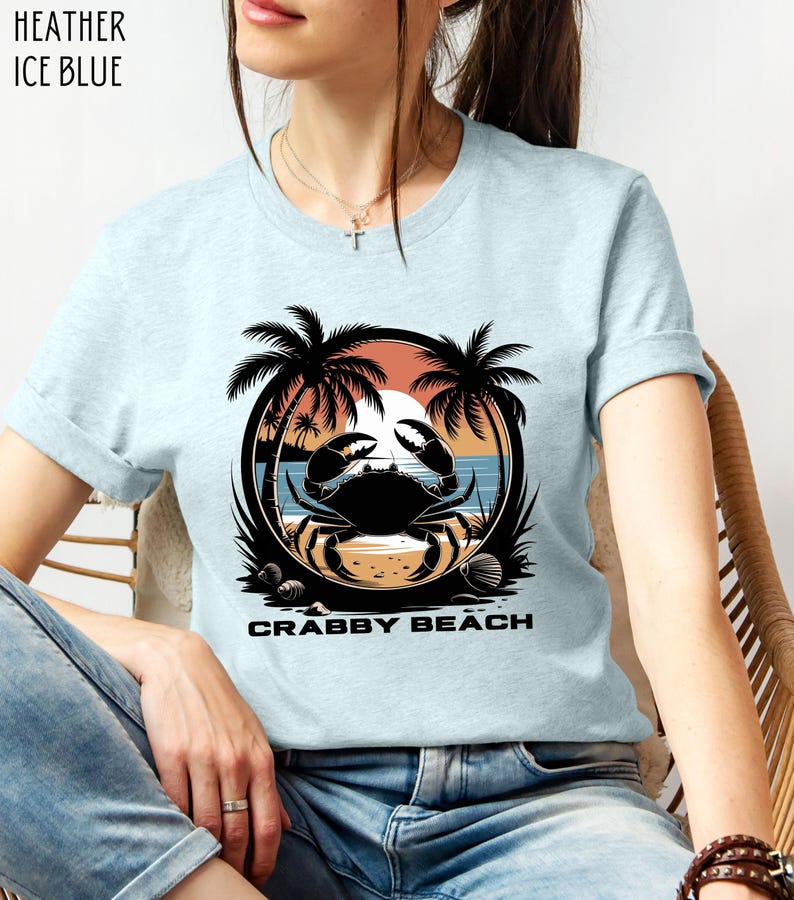 May include: A light blue t-shirt with a graphic of a crab on a beach with palm trees and the text "Crabby Beach".