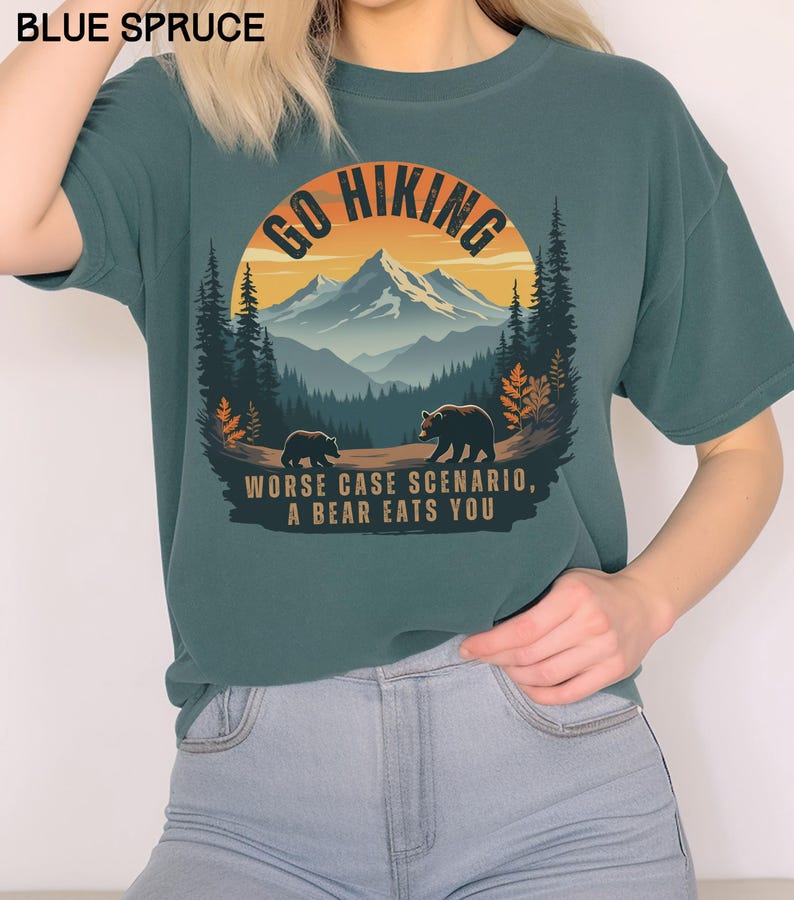 May include: A teal blue t-shirt with a graphic of a mountain range and two bears. The graphic is surrounded by a circle with the text "Go Hiking" at the top. The text "Worse case scenario, a bear eats you" is printed below the graphic.