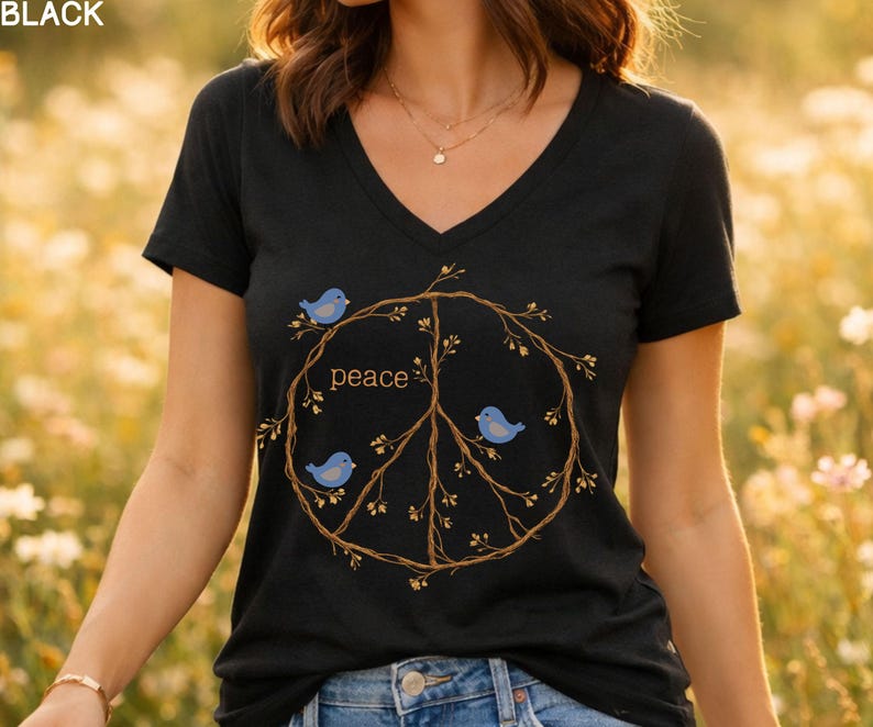 May include: Black V-neck t-shirt featuring a peace sign design made of branches, three blue birds, and the word "peace". The design is centered on the front of the shirt. The background is a field of yellow flowers.