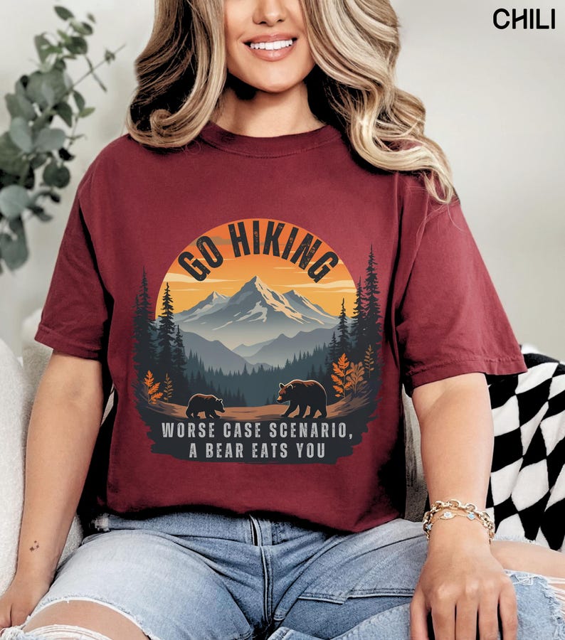 May include: A maroon t-shirt with a graphic of a mountain range and the text "Go Hiking" in a circle. Below the circle is the text "Worse case scenario, a bear eats you".