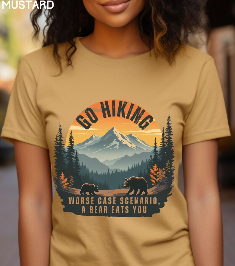 May include: A mustard yellow t-shirt with a graphic of a mountain range and two bears. The graphic is in a circle with the text "Go Hiking" above the mountain range and "Worse case scenario, a bear eats you" below the mountain range.