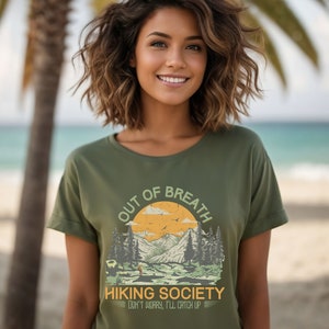 May include: A green t-shirt with a vintage-style graphic of a mountain landscape and the text "Out of Breath Hiking Society Don't worry, I'll catch up".