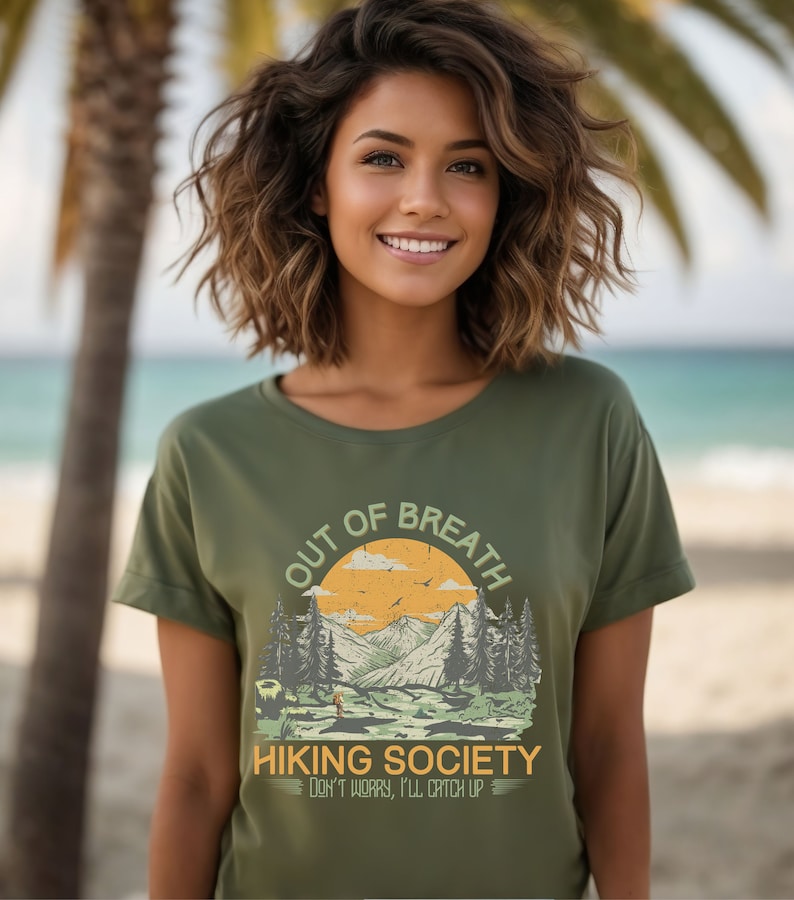 May include: A green t-shirt with a vintage-style graphic of a mountain landscape and the text "Out of Breath Hiking Society Don't worry, I'll catch up".