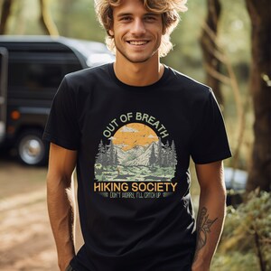 May include: A black t-shirt with a vintage-style graphic of a mountain landscape and the text "Out of Breath Hiking Society Don't worry, I'll catch up".