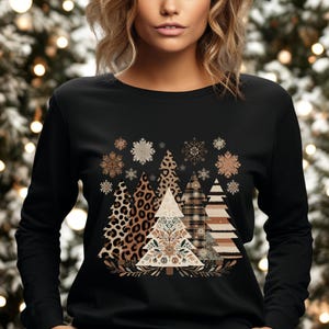 Op de afbeelding: Zwart shirt met lange mouwen met een feestelijk kerstboomontwerp. Het ontwerp bevat verschillende boompatronen, zoals luipaardprint, ruitjes en strepen, samen met sneeuwvlokken. Het woord "BLACK" staat linksboven.