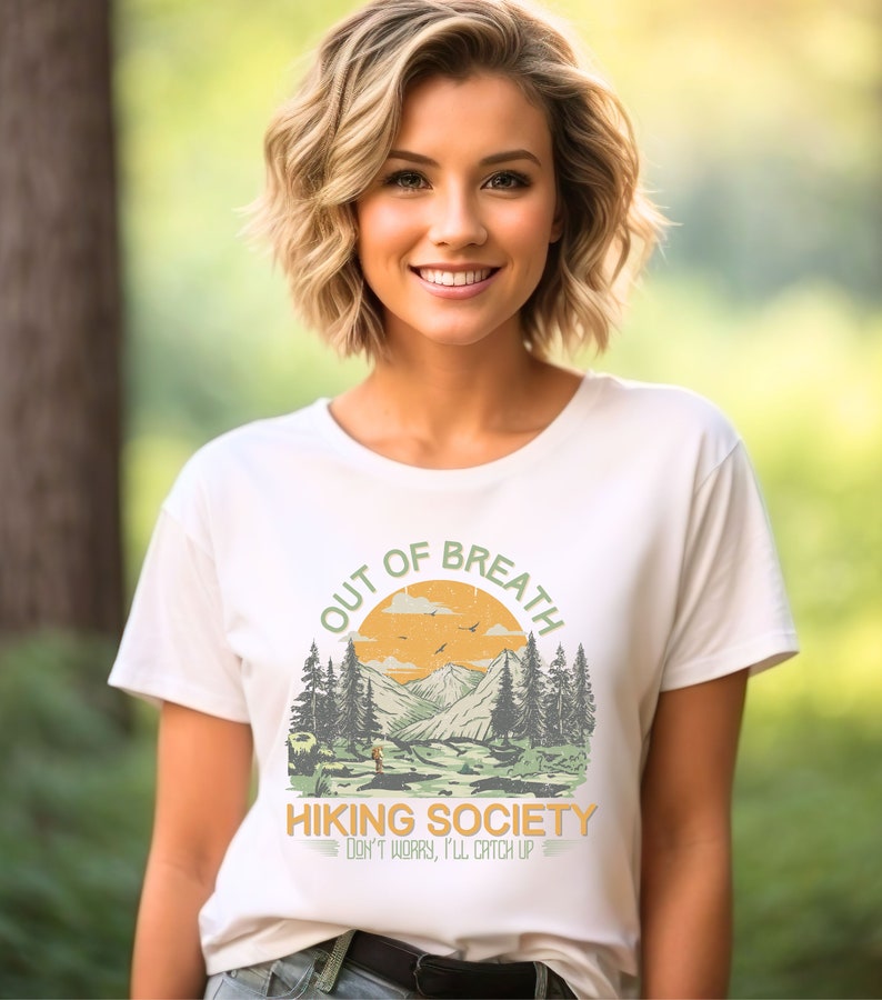 May include: White t-shirt with a graphic of a mountain landscape and the text "Out of Breath Hiking Society Don't worry, I'll catch up."