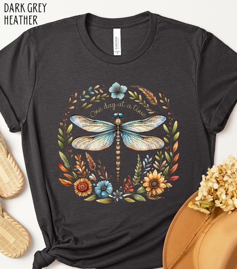 May include: Dark grey heather t-shirt with a floral design featuring a dragonfly and the text "One day at a time".