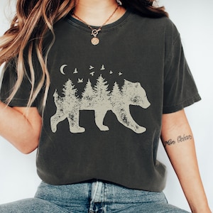 May include: A dark gray t-shirt with a graphic of a bear silhouette made up of trees and birds. The text "Mon Oc&eacute;an" is written on the right sleeve.