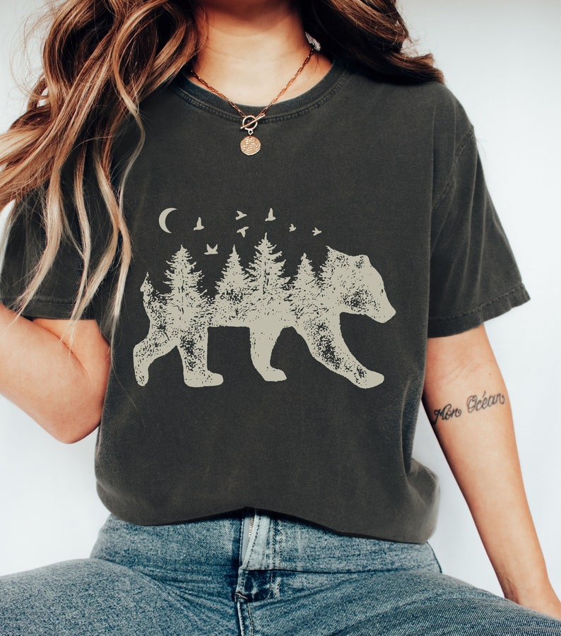 May include: A dark gray t-shirt with a graphic of a bear silhouette made up of trees and birds. The text "Mon Oc&eacute;an" is written on the right sleeve.