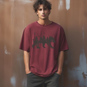 May include: A maroon t-shirt with a black graphic of a bear silhouette with trees and a crescent moon inside the bear's body.