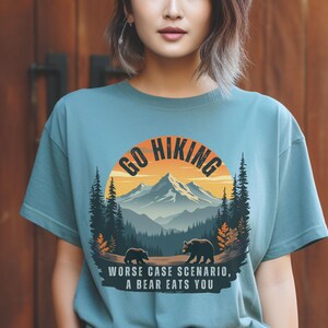 May include: A light blue t-shirt with a graphic of a mountain range and the text "Go Hiking" in a circle. The graphic also includes two bears and the text "Worse case scenario, a bear eats you".