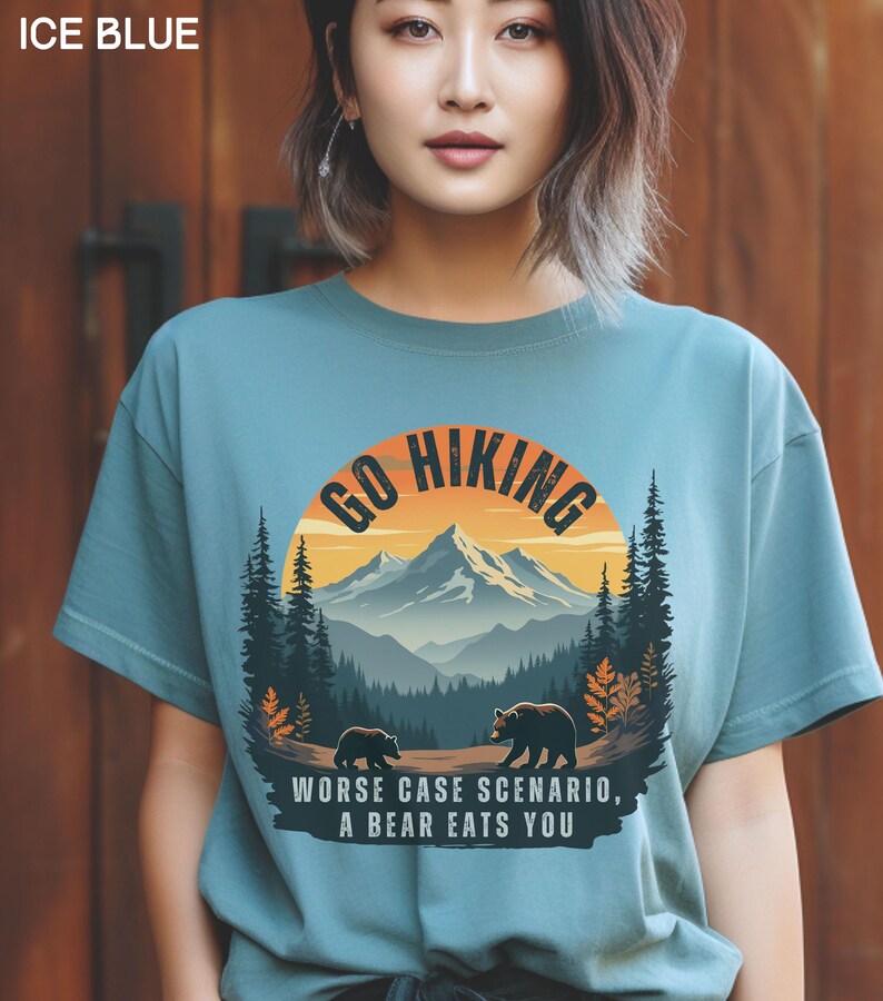 May include: A light blue t-shirt with a graphic of a mountain range and the text "Go Hiking" in a circle. The graphic also includes two bears and the text "Worse case scenario, a bear eats you".
