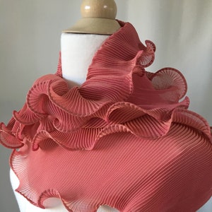 May include: A coral pink ruffled scarf made of pleated fabric. The scarf is draped around a white mannequin's neck.