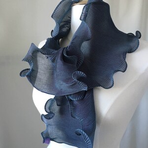 May include: A blue ruffled scarf made of pleated fabric. The scarf is draped over a white mannequin.