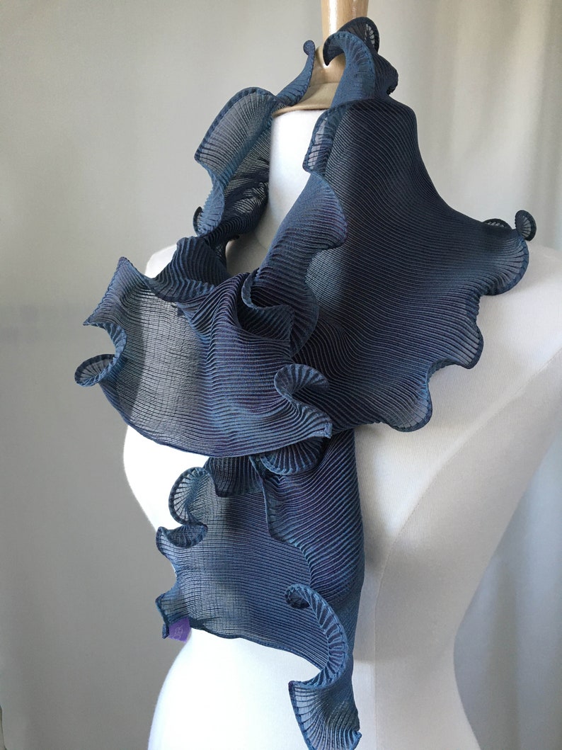 May include: A blue ruffled scarf made of pleated fabric. The scarf is draped over a white mannequin.