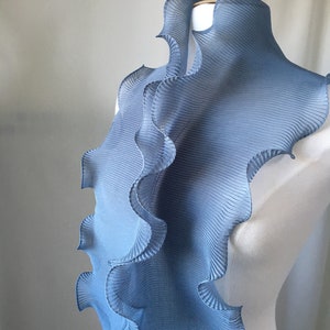 May include: A light blue pleated fabric scarf with a ruffled edge. The scarf is draped over a white dress form.
