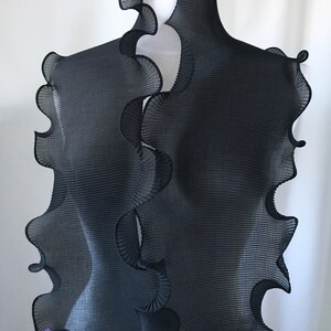 May include: Black pleated scarf with a ruffled edge. The scarf is draped over a white mannequin.