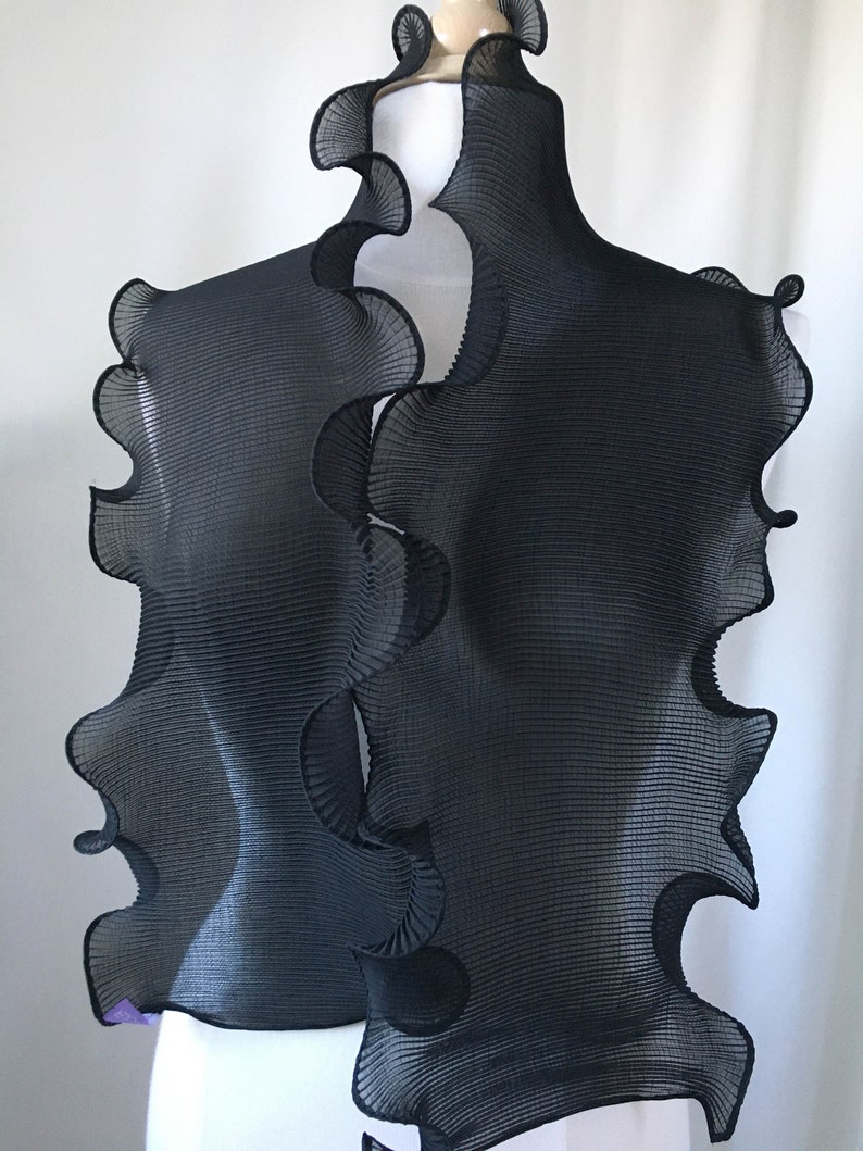 May include: Black pleated scarf with a ruffled edge. The scarf is draped over a white mannequin.