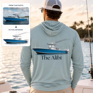 May include: A light blue long-sleeve hooded shirt featuring a graphic of a blue center console fishing boat on the back. Below the boat illustration, the text "The Alibi" is printed in a dark blue serif font. The shirt has a hood and long sleeves.