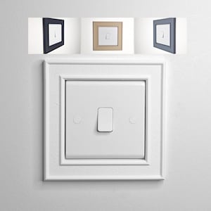 May include: A white square light switch with a decorative frame featuring a raised border. Above the main switch, three smaller inset images display the same switch design in black, beige, and grey, showcasing the variety of available frame colours.