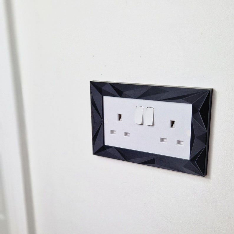 May include: A black electrical outlet cover with a geometric design. The cover has two switches and two outlets.