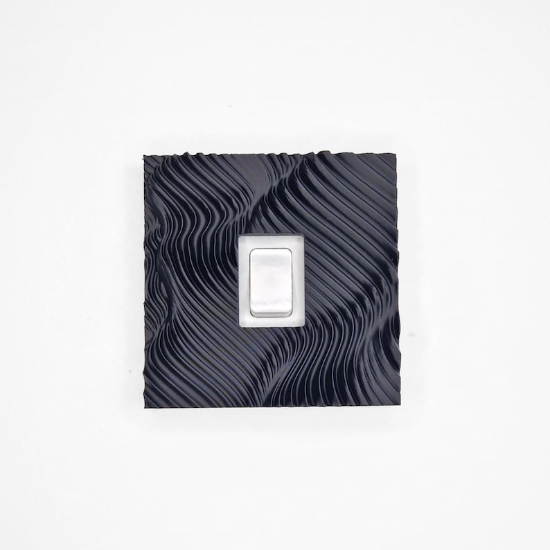 May include: A square light switch cover plate featuring a dark navy blue finish with a textured, wavy, topographical line pattern across the surface. A single, rectangular, white rocker-style light switch is centered within the plate.