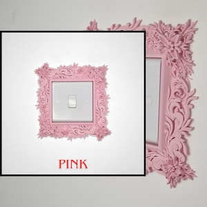 May include: A pink, ornate light switch cover with floral and scrollwork details. The cover surrounds a white light switch on a white wall. The word "PINK" is printed in red at the bottom of the image.