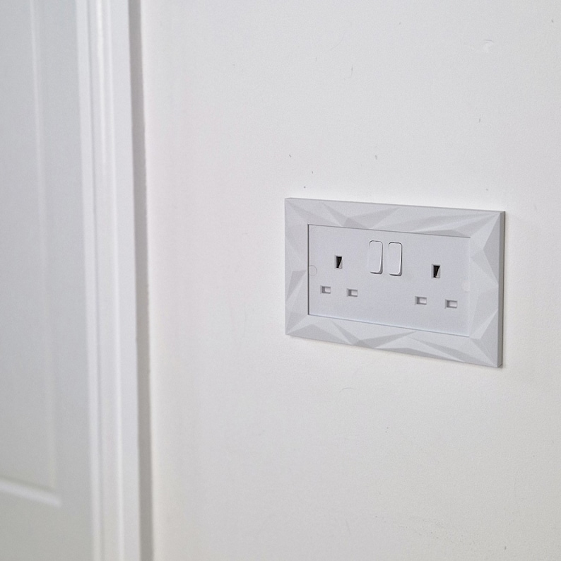 May include: White electrical outlet with two switches and two plugs. The outlet has a white, textured, geometric design.