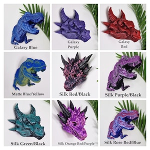 May include: Nine different colour variations of a 3D printed dinosaur and dragon figurine. The dinosaur is a Tyrannosaurus Rex and the dragon is a mythical creature with horns and spikes. The colours include galaxy blue, galaxy purple, galaxy red, matte blue/yellow, silk red/black, silk purple/black, silk green/black, silk orange red/purple, and silk rose red/blue.