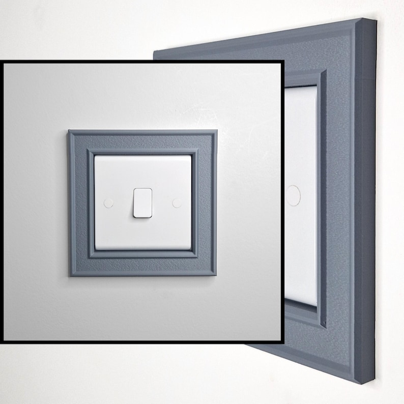 May include: A white light switch featuring a rectangular toggle mechanism, centered within a square, textured slate-gray decorative frame. The frame has a beveled edge design that surrounds the switch plate, providing a distinct border.