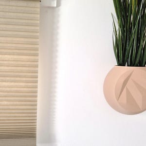 May include: A light pink, geometric, wall-mounted planter with a green plant inside.