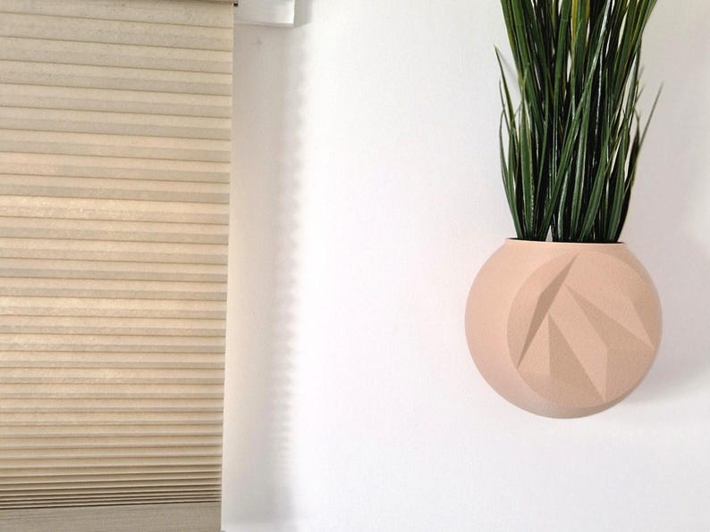 May include: A light pink, geometric, wall-mounted planter with a green plant inside.