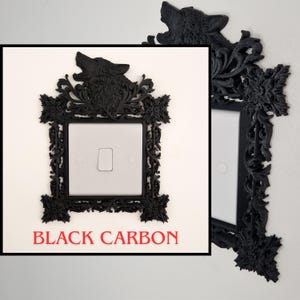 May include: Black carbon fiber light switch cover with a decorative frame. The frame features a howling wolf at the top and ornate floral and scrollwork designs. The text "BLACK CARBON" is displayed in red at the bottom.