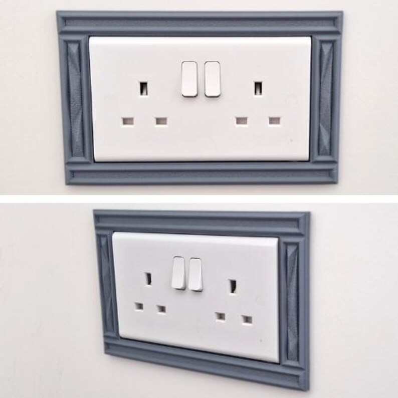 May include: A white double electrical wall outlet with two switches, framed by a decorative gray rectangular border featuring a textured, molded edge design. The outlet is shown from both a direct front view and an angled perspective.