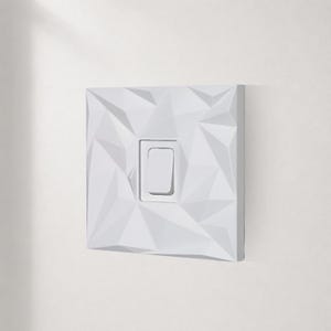 White geometric self adhesive light switch cover installed on a modern textured wall.