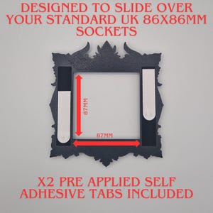 May include: A black decorative frame with ornate edges, designed to fit over UK 86x86mm sockets. The frame measures 87mm by 87mm internally and includes two pre-applied self-adhesive tabs. Text on the frame reads "DESIGNED TO SLIDE OVER YOUR STANDARD UK SOCKETS".