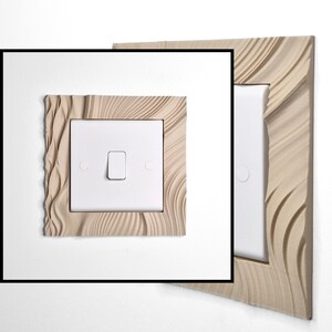 May include: A square light switch cover plate featuring a beige, textured frame with flowing, wave-like patterns surrounding a central white rectangular switch. The design includes a smooth white center toggle and two circular screw covers on the sides.