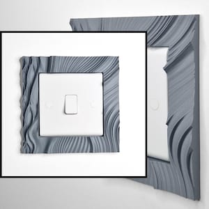 May include: A white single light switch featuring a decorative grey frame with a textured, wavy, and rippled surface pattern. The frame surrounds the square switch plate, which includes a central toggle and two circular screw covers on the sides.